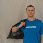 Volunteer in blue shirt holding a garbage bag during a cleanup effort.