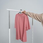 A pink t-shirt hangs on a rack held by a person, ideal for mockups and fashion design.