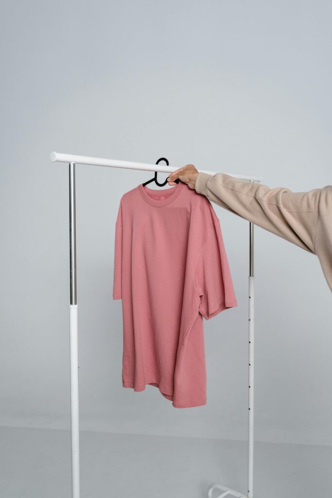 A pink t-shirt hangs on a rack held by a person, ideal for mockups and fashion design.